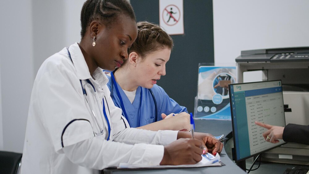 Multiethnic team of specialists analyzing report papers at hospital reception desk in lobby, helping people with appointments. Doctor and nurse using medical forms with checkup. Handheld shot.